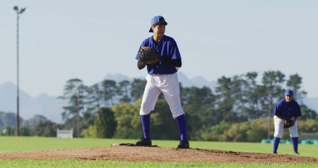 Pitcher preparing to throw ball during baseball game on outdoor field, teammate in background playing defense, ideal for sports articles, profiles, and tutorial content related to baseball techniques