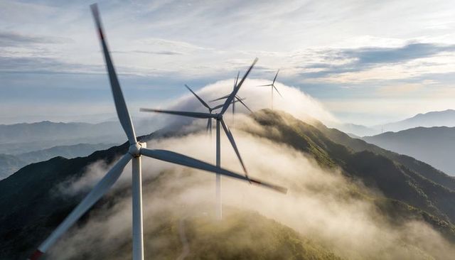 Wind turbines spinning along foggy mountain ridge at sunrise over valleys