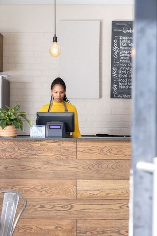 African american barista working at modern wooden cafe counter with pos terminal