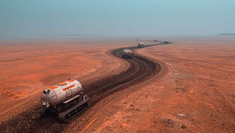 Convoy of tracked tanker vehicles carving winding rut across red desert expanse