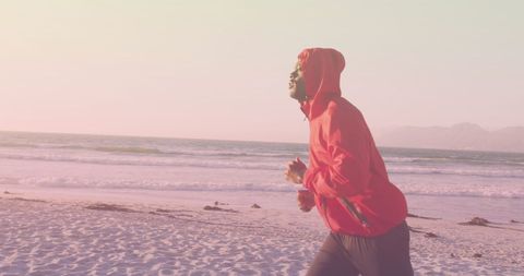 Man Jogging Along Beach in Red Hoodie at Sunrise