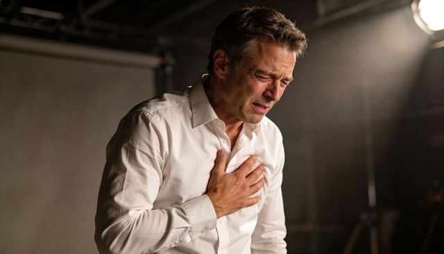 Middle-aged man clutching chest, experiencing pain during dramatic acting performance in studio