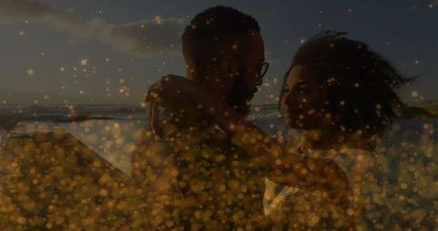 Couple embracing at sunset on beach with golden bokeh and backlit silhouette