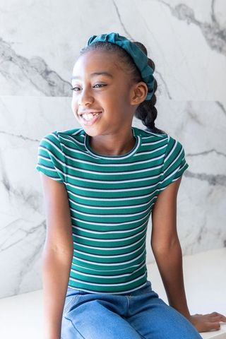 Smiling african american girl sitting on white bench wearing teal headband and striped top