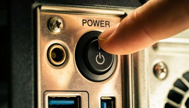 Fingertip pressing power button on desktop pc rear panel closeup with usb 3.0 ports