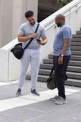 Two male friends in sportswear checking smartphone together on urban plaza steps