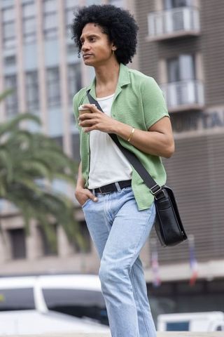 African american man walking with coffee and satchel in urban street style