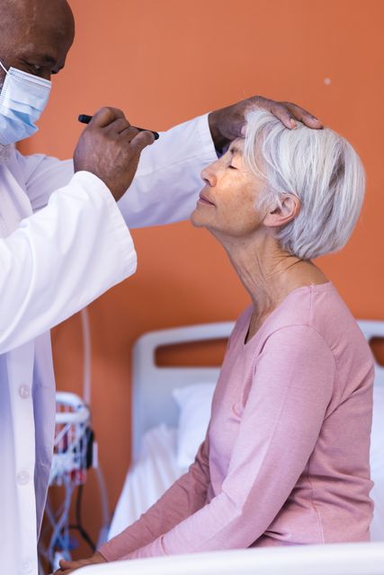 This image depicts a healthcare professional examining the eye of a senior patient using a penlight in a hospital setting. It is ideal for use in medical articles, healthcare brochures, senior care advertisements, and educational materials about patient care and health checkups.