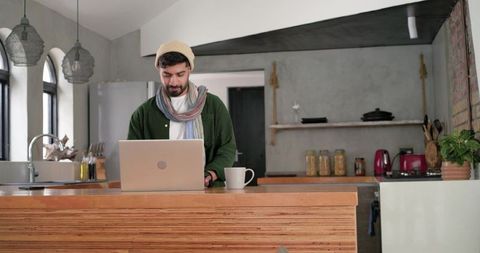 Indian man working remotely on laptop at cozy modern rustic kitchen island