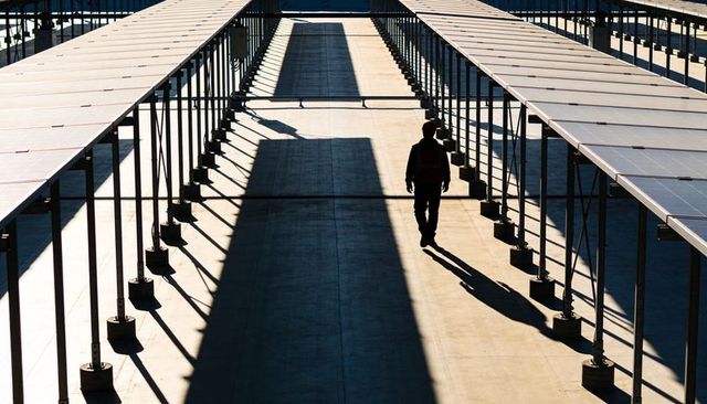 Walking silhouetted technician inspecting solar panel arrays on concrete corridor