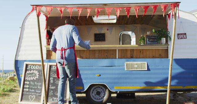 Rear view of african american man wearing apron smiling while cleaning the food truck. food truck and street food concept