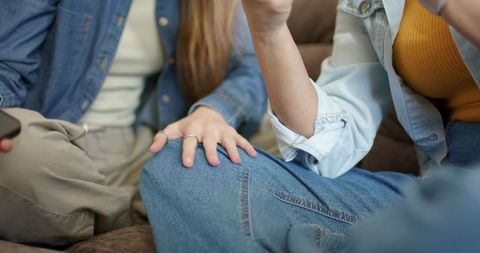 Diverse women chatting and relaxing on brown couch in denim and casual outfits