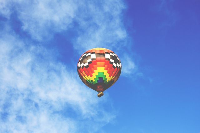 Bright and colorful hot air balloon floating through clear blue sky. Suitable for travel brochures, adventure advertisements, and motivational posters encouraging exploration and open skies.