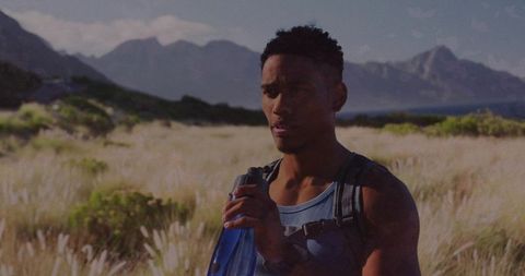Hiker sipping water in coastal meadow with backpack and mountain views