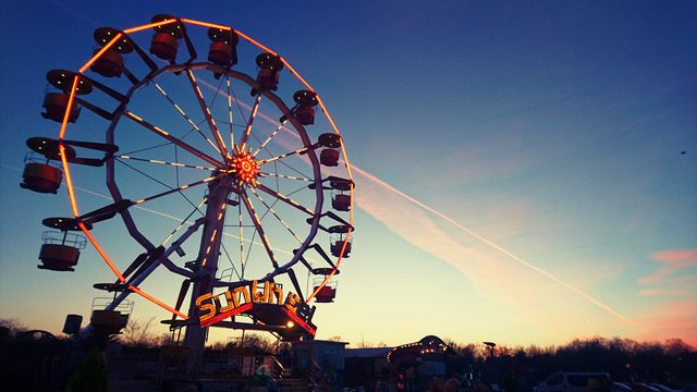 Brightly illuminated ferris wheel in amusement park during sunset. Glowing against twilight sky, creating relaxing evening atmosphere perfect for theme park marketing, travel, family entertainment. Ideal for evoking nostalgia and fun vibes in advertisements or travel brochures.