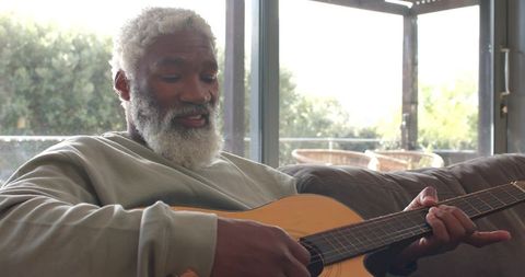 Senior Man Relaxing on Sofa Playing Acoustic Guitar in Sunlit Living Room