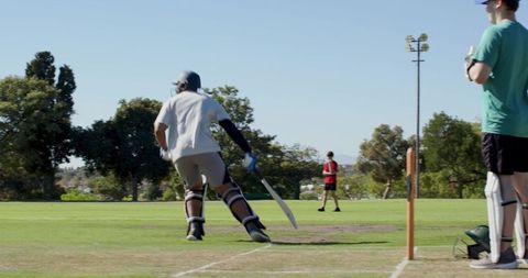 Adult batsman batting on sunny park cricket pitch wearing helmet and pads