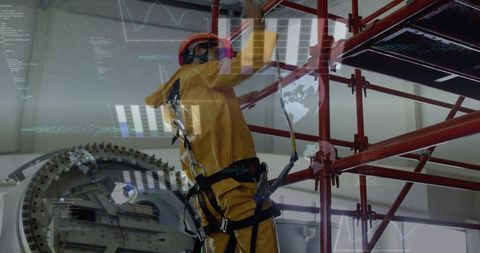 Industrial technician climbing red scaffold in yellow safety suit using fall-arrest harness