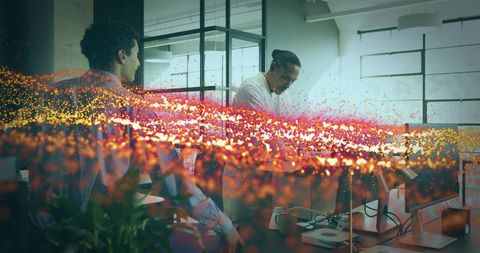 Two colleagues collaborating over desk with warm particle light overlay in modern office