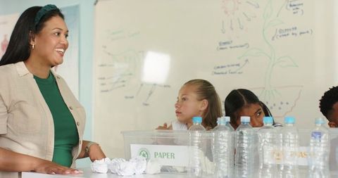 African American teacher guiding students in recycling lesson with paper and bottles