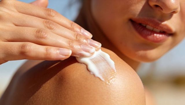 Woman applying sunscreen on sunlit shoulder at beach, skin care and sun protection