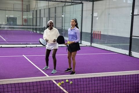 Two women holding padel rackets and balls on vibrant purple indoor court