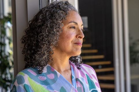 Senior african american woman gazing through window in colorful shawl, serene contemplation
