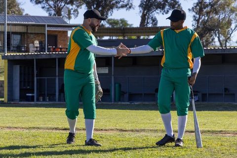Baseball Teammates Exchanging Handshake on Sunlit Field Wearing Green Yellow Uniforms