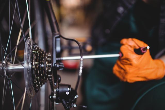 Mechanic working on bicycle gears using professional tools in a workshop. Ideal for illustrating bicycle maintenance, mechanical services, or workshops. Perfect for articles, advertisements, or websites related to cycling, bike repair, or mechanical services.