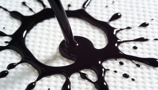 Pouring glossy black liquid forming radial splash on white waffle-weave fabric