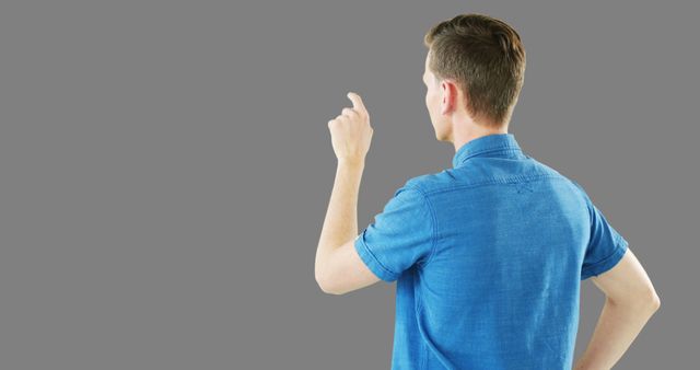 Man in blue shirt pointing at invisible object, seen from back view, ideal for tech tutorials, advertising, presentations, user interface demonstrations, or educational materials.