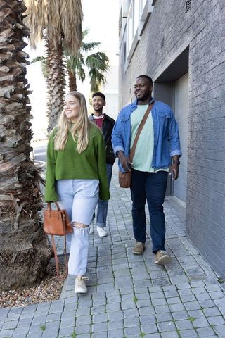 Diverse friends walking on urban sidewalk with palm trees, smiling and carrying bags