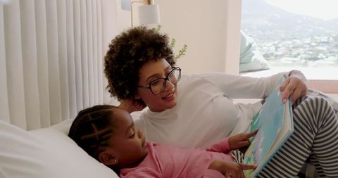 Mother and Daughter Reading Book Together on Bed Relaxing