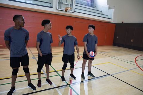 African american teen teammates preparing for volleyball match on indoor gym court