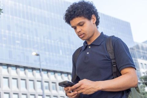 African american man checking smartphone outside corporate glass building with backpack