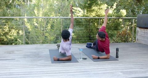 Diverse friends performing outdoor side plank on wooden deck