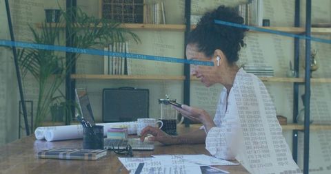 Focused woman multitasking with laptop and smartphone amid home office setup