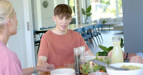 Teen boy chatting at family dining table casual sunlit open-plan lunch with salad