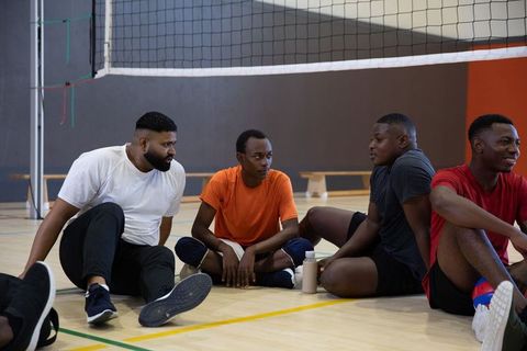 African american teammates resting and chatting after indoor volleyball match in gymnasium