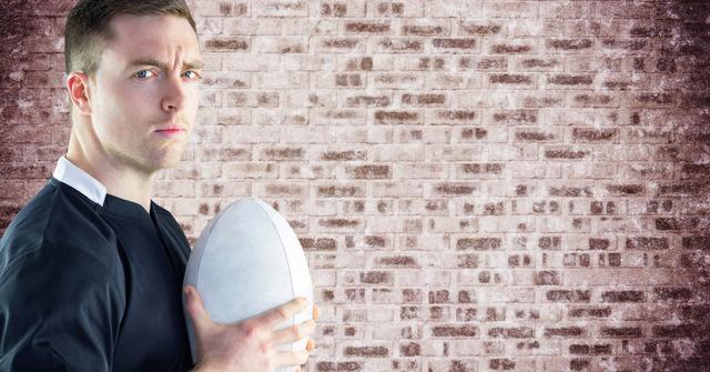 Rugby player holding ball with serious expression, standing against a weathered brick wall. Ideal for use in sports advertising, team promotions, fitness inspiration, and athletic company branding.