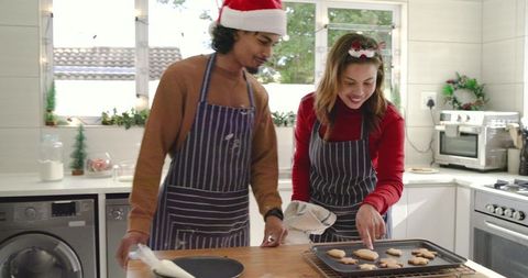 Couple Decorating Christmas Cookies in Cozy Kitchen Wearing Striped Aprons and Santa Hats