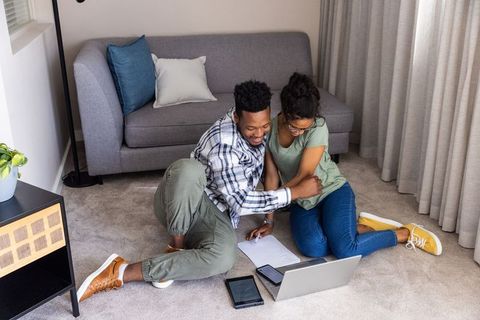 Young diverse couple planning finances and collaborating with laptop on living room floor
