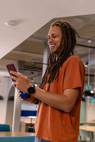 African American man laughing while checking phone in modern coworking space
