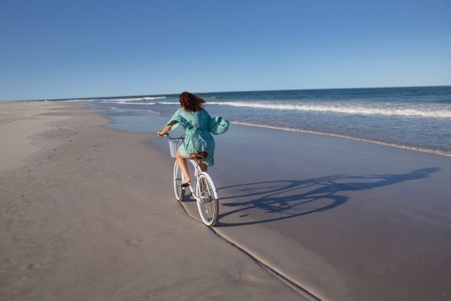 Rear view of biracial woman riding bicycle on beach in the sunshine