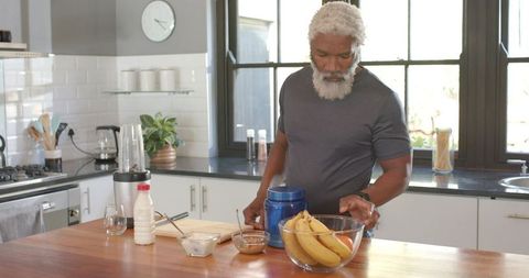Senior man preparing healthy smoothie ingredients in modern kitchen