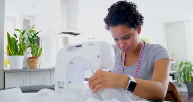 Woman concentrates on sewing using a sewing machine at home. Perfect for illustrating topics related to crafting, tailoring, creativity at home, learning new skills, or DIY projects and hobbies.