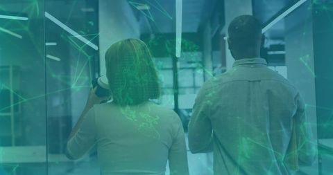 Colleagues walking down glass corridor holding coffee and folder with network overlay