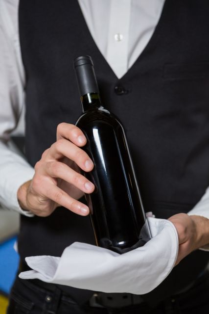 Bartender holding wine bottle wrapped in white cloth, showcasing professional service in an elegant bar. Ideal for use in hospitality industry promotions, restaurant advertisements, and service training materials.