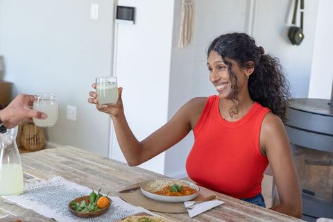 Smiling african woman toasting with companion over lemonade at cozy wooden dining table