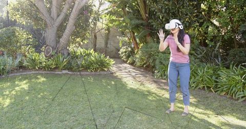Woman exploring virtual reality in sunny backyard garden wearing white vr headset
